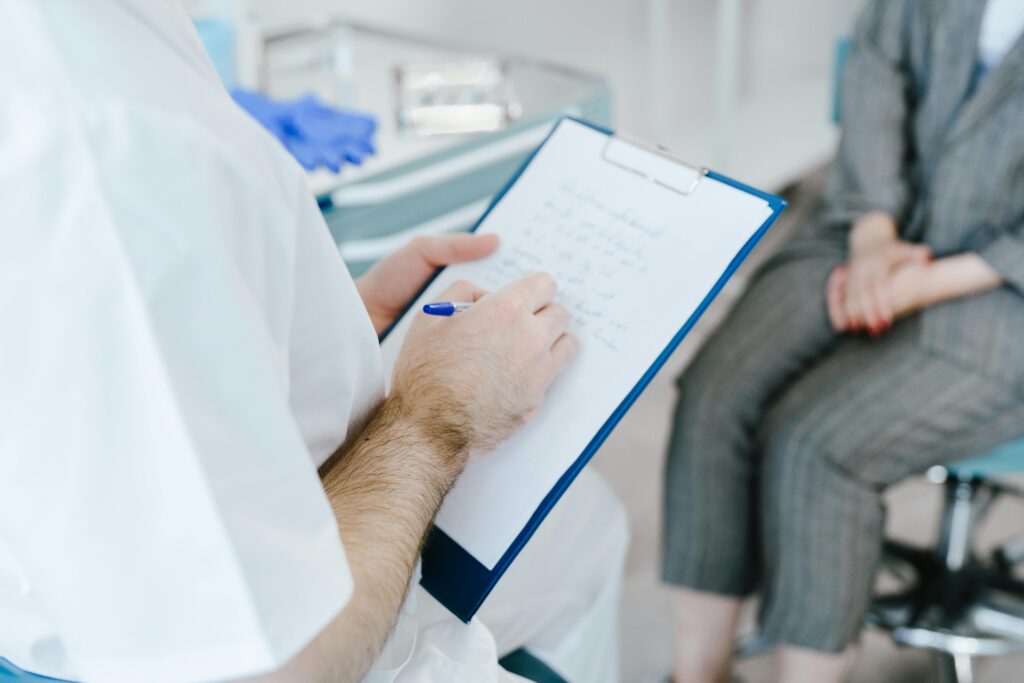 Doctor taking notes with a patient in an exam room.